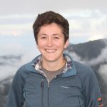 Sarah Fitzpatrick stands, smiling, in front of a mountain range.