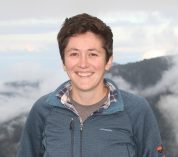 Sarah Fitzpatrick stands, smiling, in front of a mountain range.