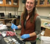 Heather Kittredge stands in a laboratory, smiling at the camera.
