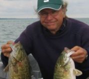 Doug Schemske sits on a fishing boat holding a pair of smallies.