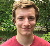 Tyler Treakle, wearing a red T-shirt, stands outside smiling at the camera.