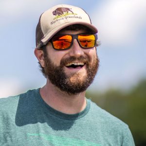 Sean Griffin, wearing sunglasses and a baseball cap, smiles for an outdoor portrait.