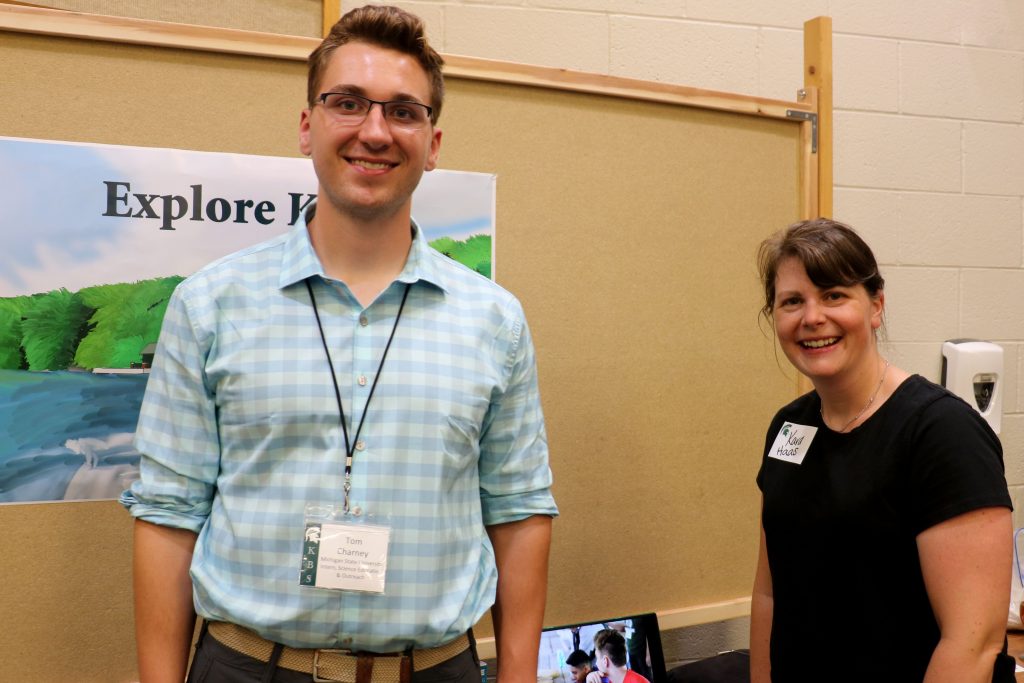Tom  Charney stands in front of his poster project, smiling with his mentor, Kara Haas.