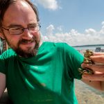 Brendan Reid poses holding three small turtles.