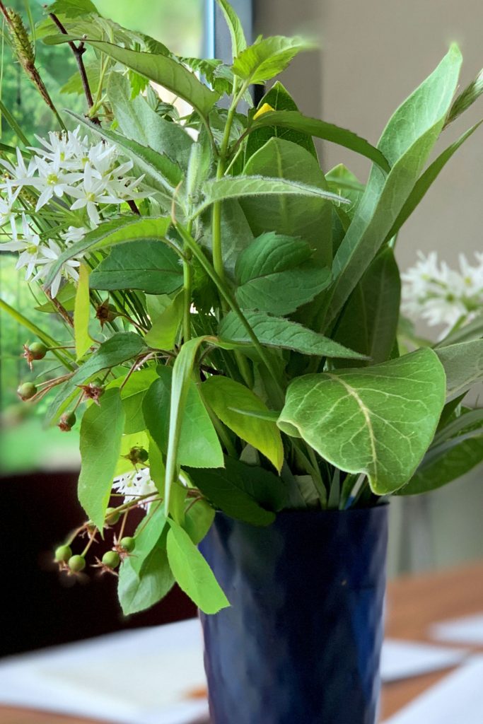 Plants including milkweed are arranged in a vase sitting on a table.