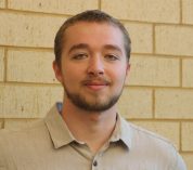 Portrait of Kyle Jaynes standing in front of a brick wall.