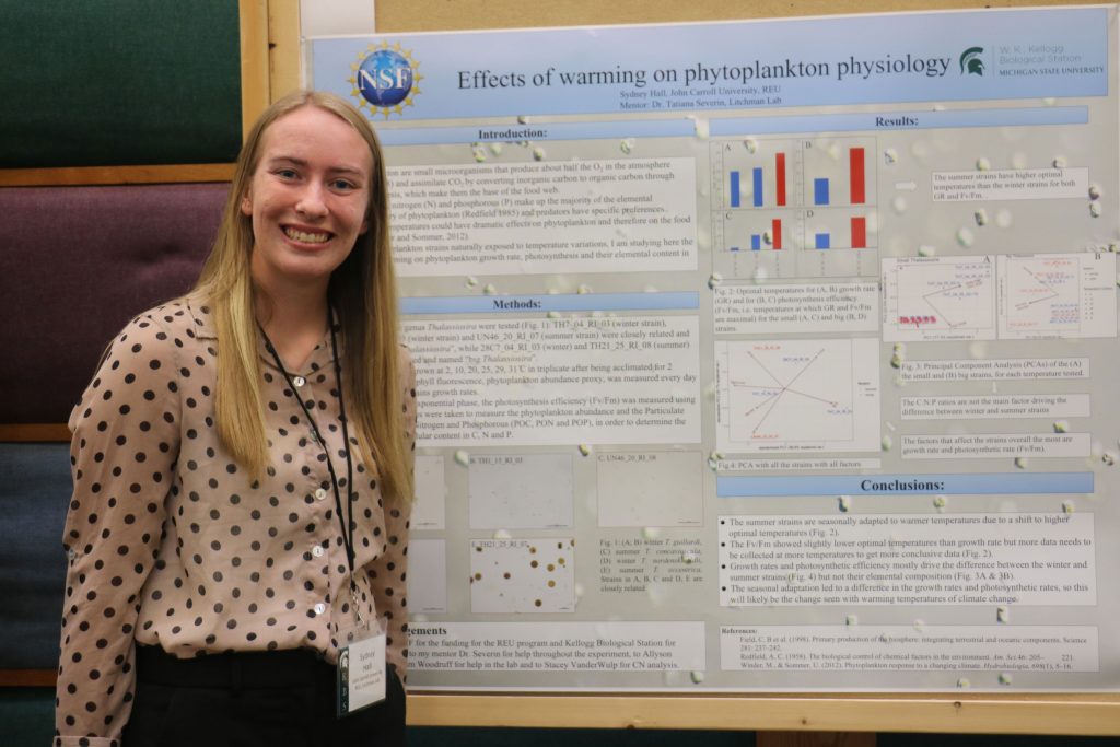 Sydney Hall stands, smiling, next to her research poster at the KBS undergraduate research symposium.