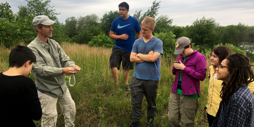 Dr. Fredric Janzen speaks to a group of students outside while holding a snake.
