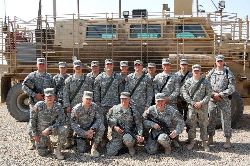 A group of members of the U.S. Army, including Jim Allen, pose for a photo in front of a military vehicle.