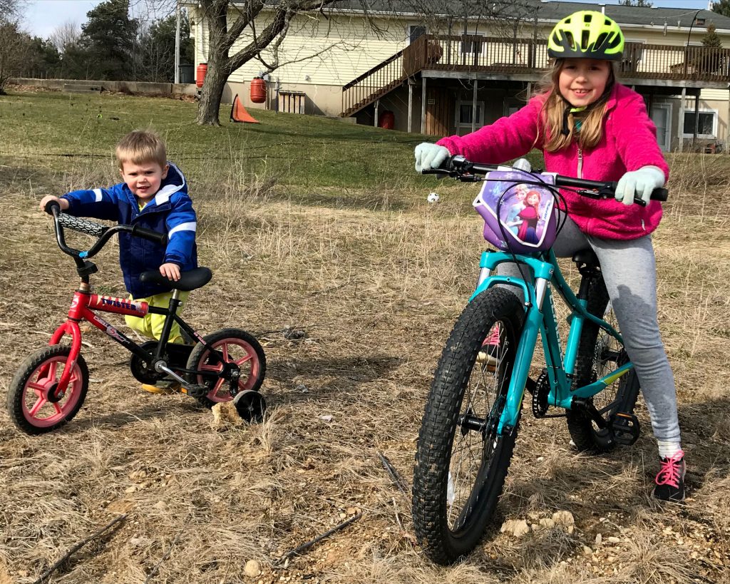 Children on bikes pose in a field in early spring.