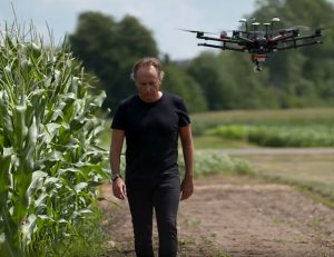 Bruno Basso walks next to a cornfield while a drone flies overhead.