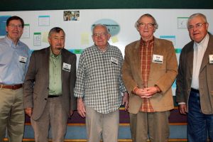 Five men stand shoulder to shoulder in from of a research poster, with Don Hall second from right.