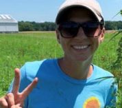 Alyssa Schuck stands in a field, smiling and making a peace sign.