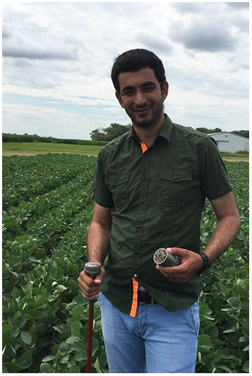 Ekrem Ozlu stands in a soybean field holding a soil sample.