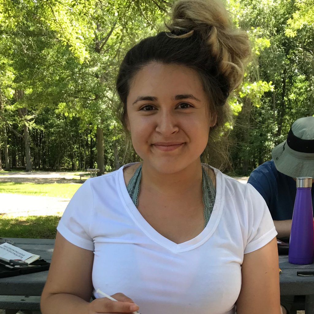 Victoria Villanueva smiles at the camera while seated against a backdrop of trees.