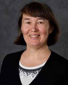  Portrait of Elena Litchman, wearing a black and white shirt against a neutral background.