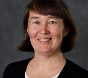 Portrait of Elena Litchman, wearing a black and white shirt against a neutral background.