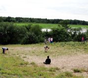 Members of the Janzen Lab work on a grassy hilltop with trees and water in the background.
