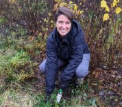 Isabela Borges crouches in a field at the KBS Long-term Ecological Research site, using a trowel to dig up plants.