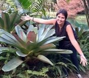 Isabela Borges poses with arms outstretched to show the size of the large plant next to her.