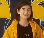 Katherine Egeler, wearing a black T-shirt with a Monarch butterfly image, stands against a black and yellow mural of a butterfly.