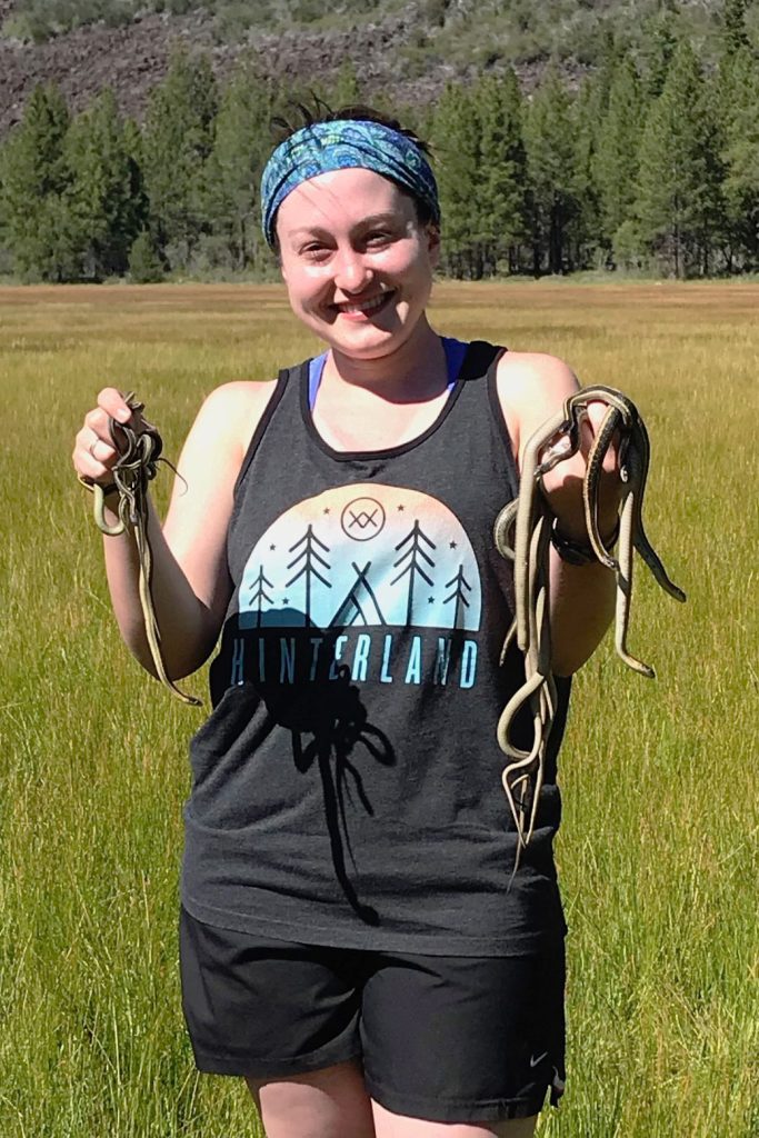 Jessica Judson stands in a field holding several snakes.