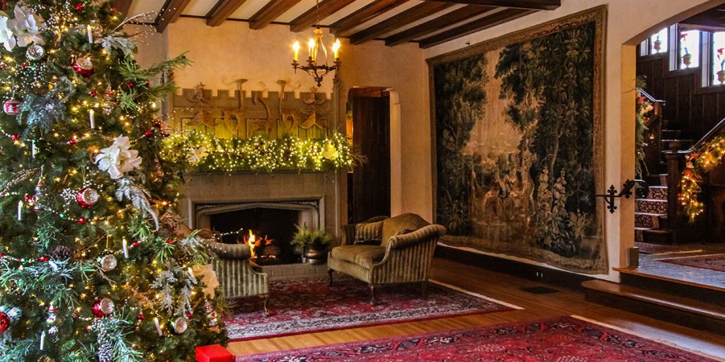 A decorated Christmas tree stands in the corner of the W.K. Kellogg Manor House living room, with a red area rug and fireplace in the background.