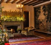 A decorated Christmas tree stands in the corner of the W.K. Kellogg Manor House living room, with a red area rug and fireplace in the background.