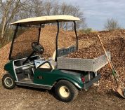 A green golf cart donated to the Kellogg Bird Sanctuary sits next to a large pile of wood chips, with a shovel leaning against the bed of the cart.