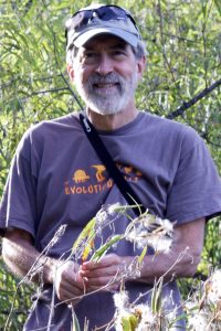 Jeff Conner stands among plants, holding several fluffy seed pods.