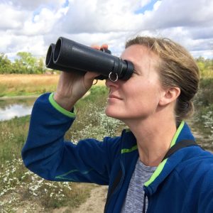 Kristy Taylor peers through binoculars upward toward the sky.