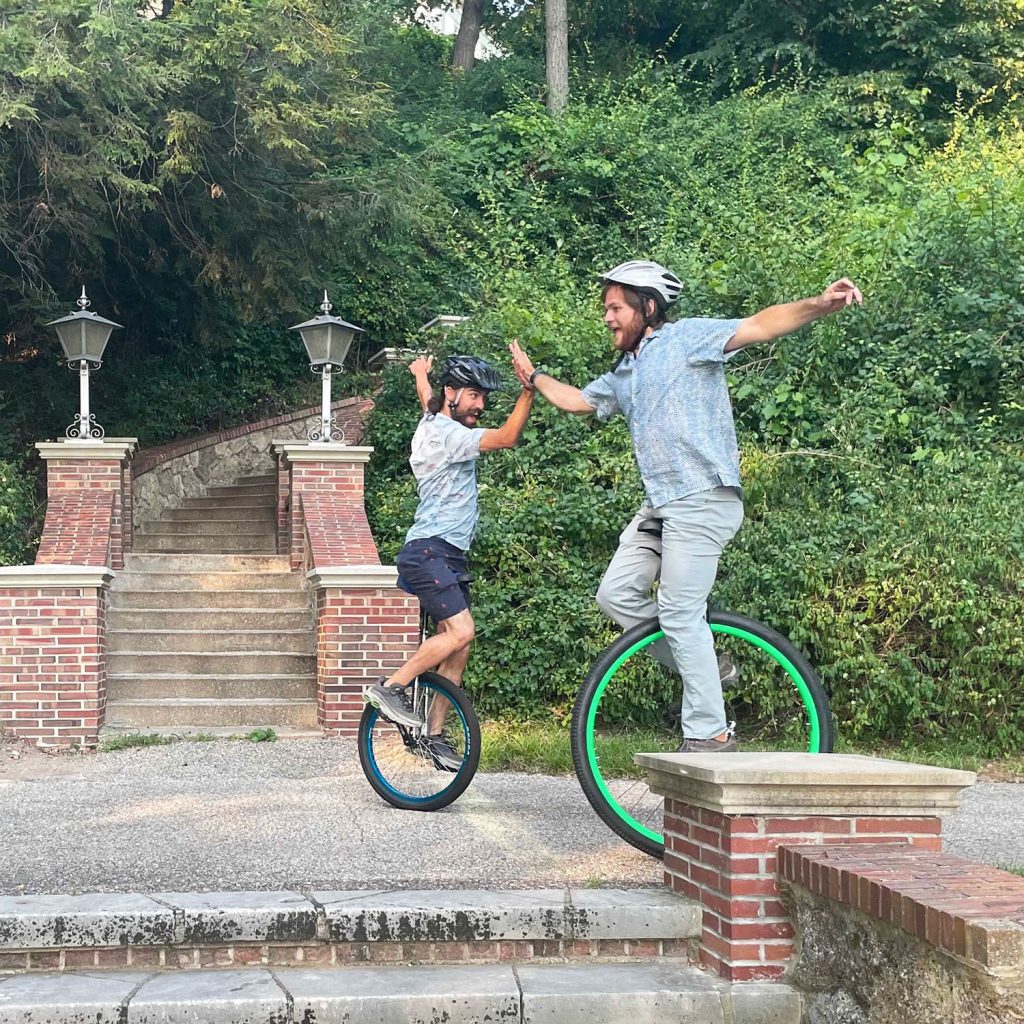 Bjorn Larson and Joseph Savage ride unicycles on the sidewalk near the Manor House pagoda at KBS.