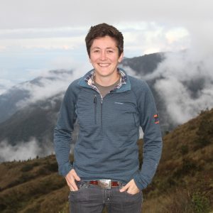 Sarah Fitzpatrick stands in front of a mist-covered mountain range.