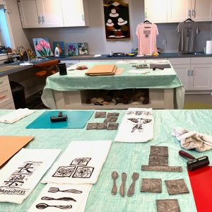 Supplies used for block print projects along with some finished items lie on a table.