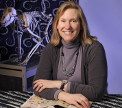 Head shot of Anne Bronikowski seated at a table with a stack of magazines.