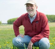 Phil Robertson smiles at the camera while crouching in an agricultural field at KBS.