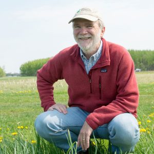 Phil Robertson smiles at the camera while crouching in an agricultural field at KBS.