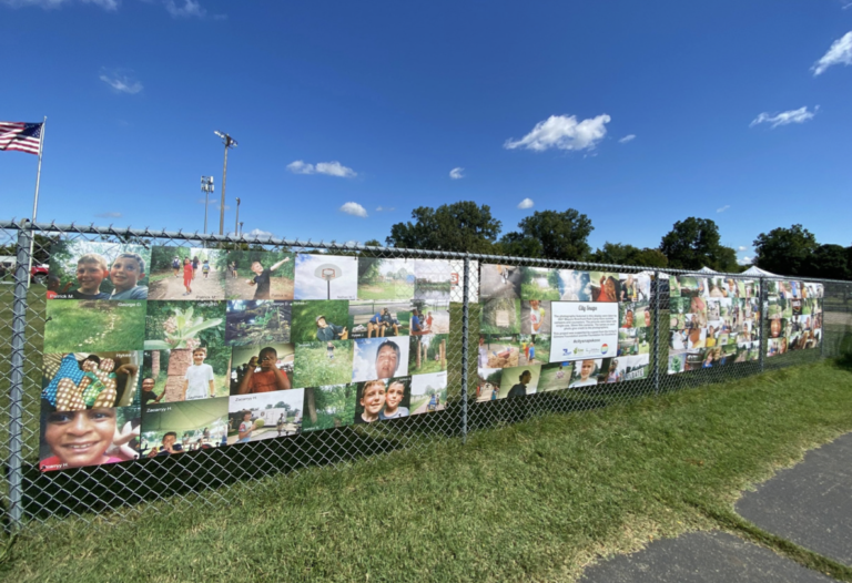 Dream Scene Placemaking’s City Snaps public art display, consisting of photographs taken by summer camp children printed into a collage and mounted on a chain-link fence in Kalamazoo.