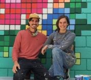 Erik Vasilauskas and Anna Lee Roeder kneel in front of an in-progress mural of colorful blocks.