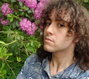 2022 W.K. Kellogg Bird Sanctuary visitor experience intern Ezra Montero poses near a blooming rhododendron bush.