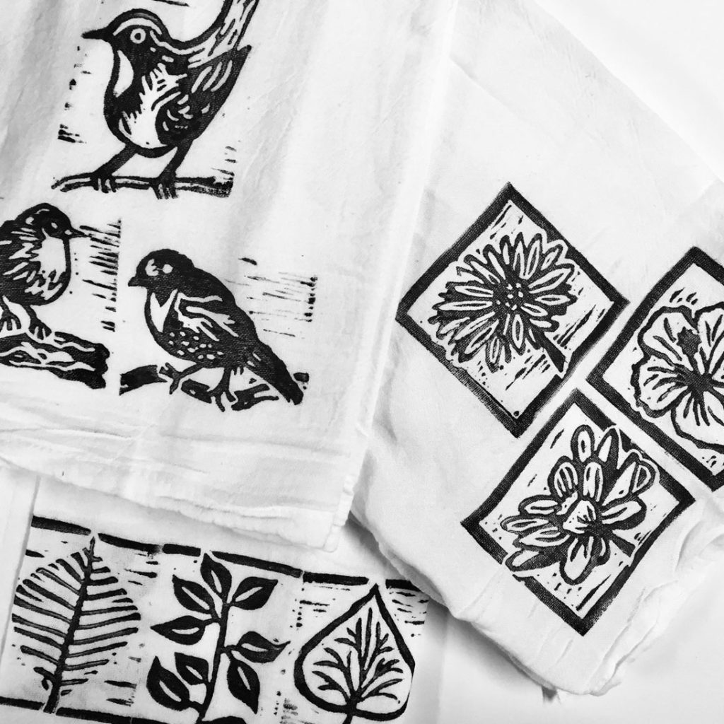Block prints of birds and plants are shown in black ink on white tea towels.