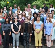 W.K. Kellogg Biological Station 2022 summer students and mentors pose for a group photo on a set of stairs with trees in the background.