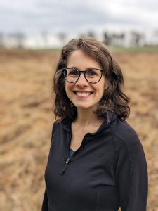 Head shot portrait of Tayler Ulbrich against the background of an agricultural field.