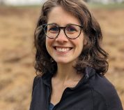 Head shot portrait of Tayler Ulbrich against the background of an agricultural field.