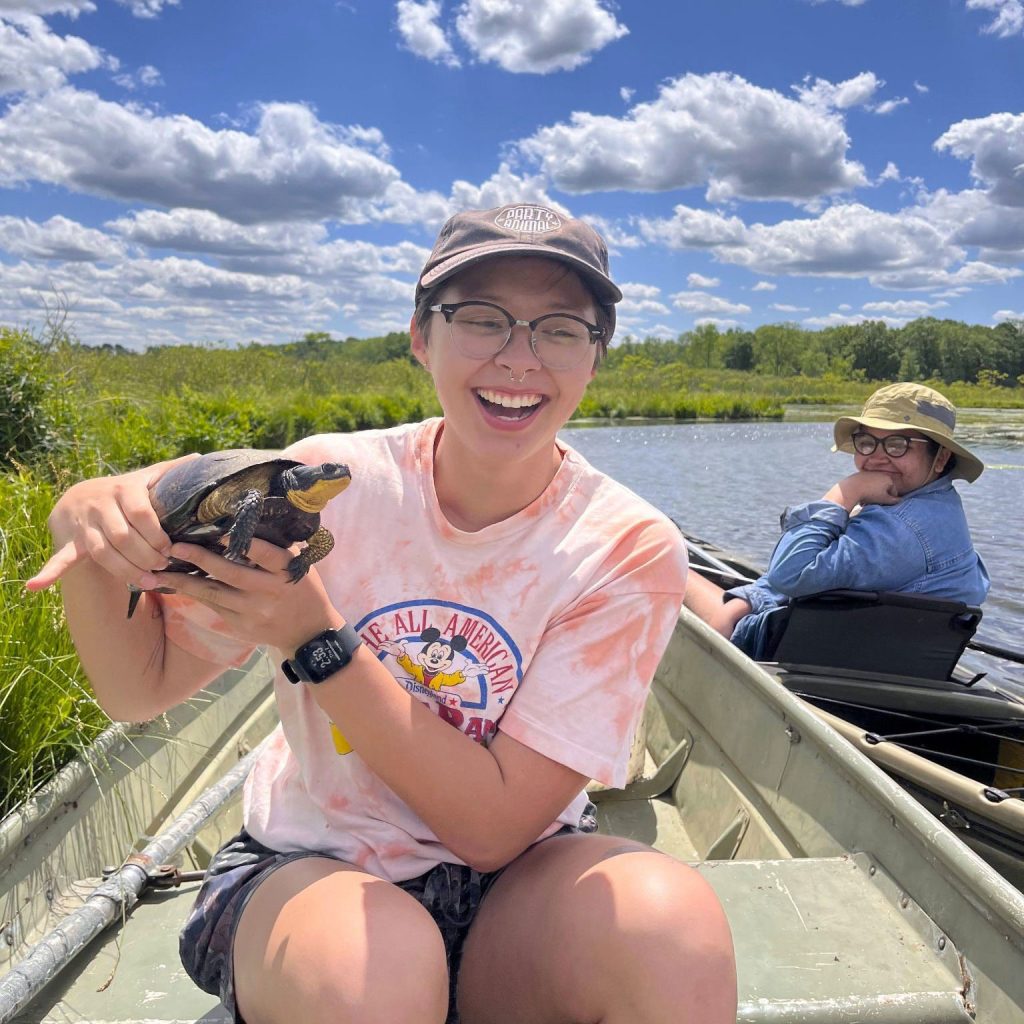 Sofie Iwamasa holds a turtle while sitting in a canoe on a sunny day.