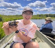 Sofie Iwamasa holds a turtle while sitting in a canoe on a sunny day.