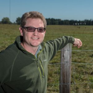 Dr. Jason Rowntree leans on a fence post in front of a pasture.