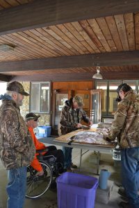 A group of volunteers wearing hunting camouflage gather around a table, cleaning and filleting fish.