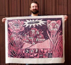 Trevor Grabill holding one of their prints created by stamping and layering designs from hand-carved wooden blocks.