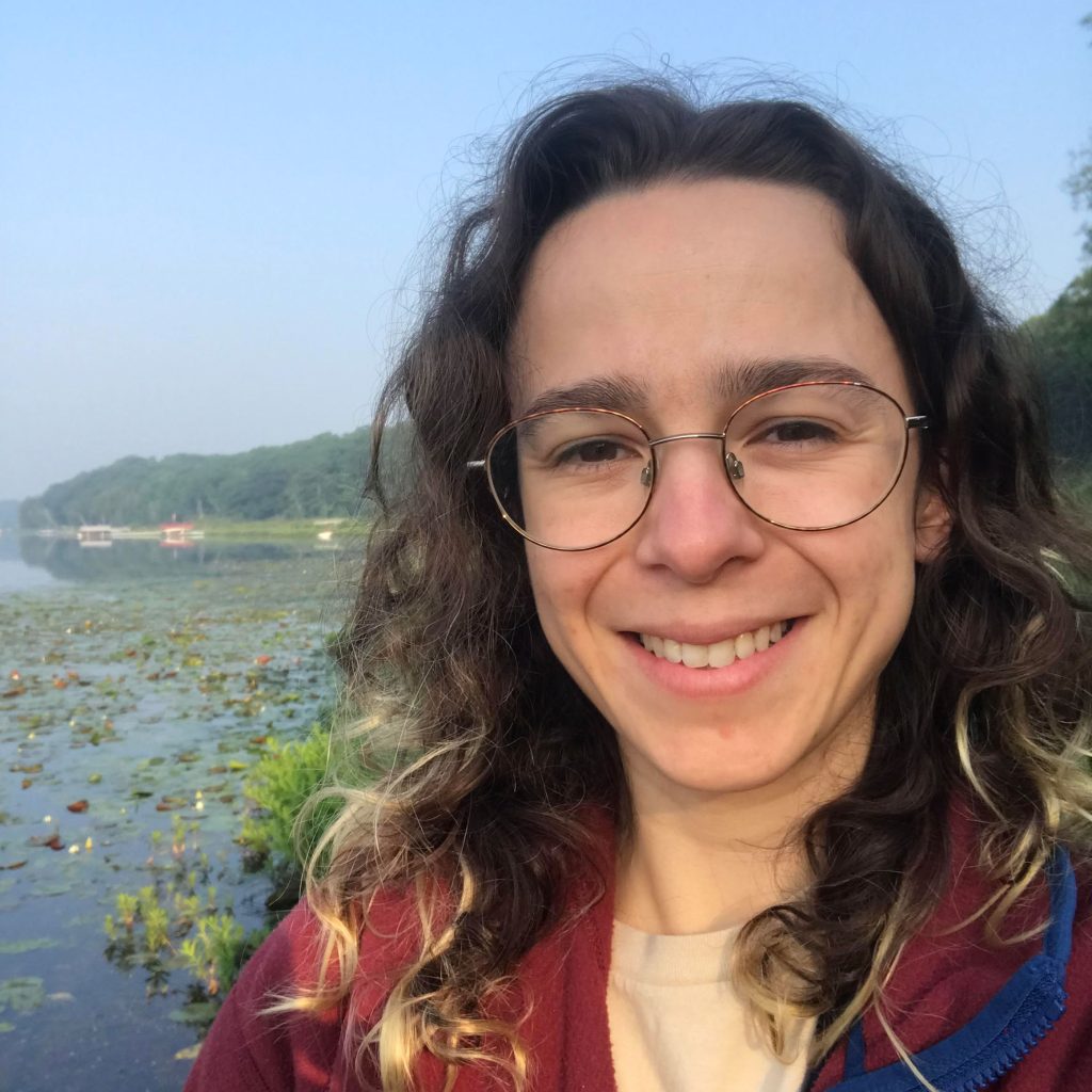 Head shot photo of Claudia Crowther, with a small lake with boat docks in the background.